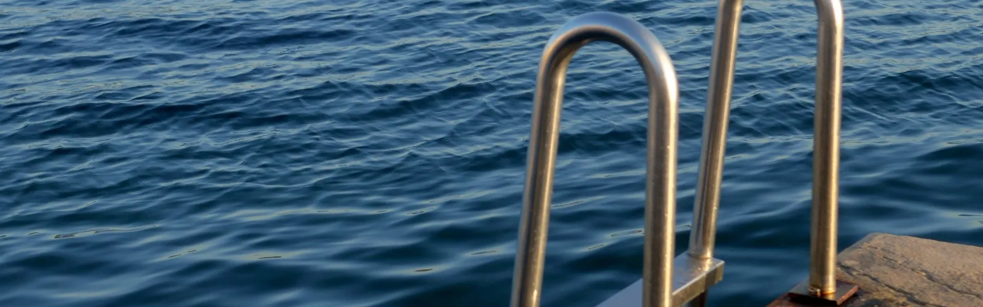 Stainless steel swimming ladder on a pontoon leading to a slightly choppy blue sea