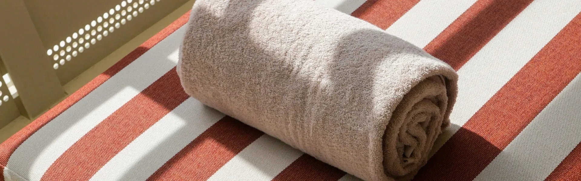 A rolled beige bath towel lying on a terracotta and white striped sun lounger in the sun