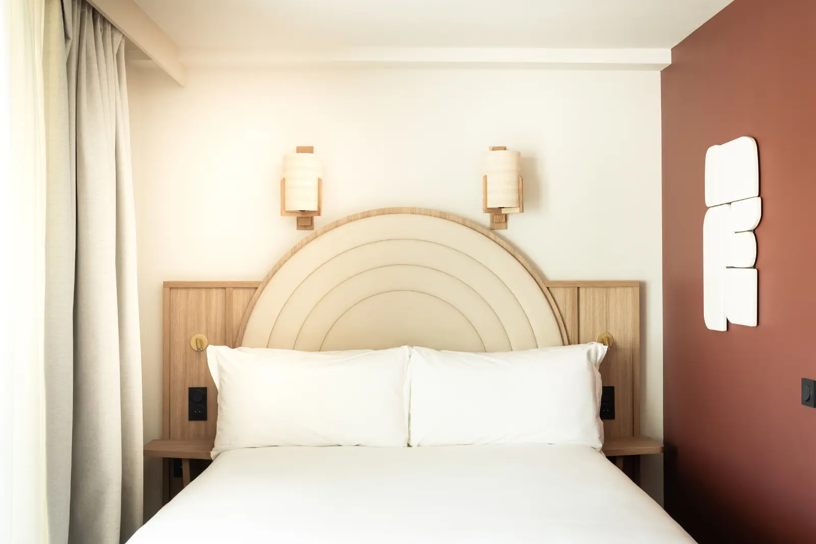 Hotel room with a double bed, a curved rattan headboard, wall lights and a terracotta feature wall