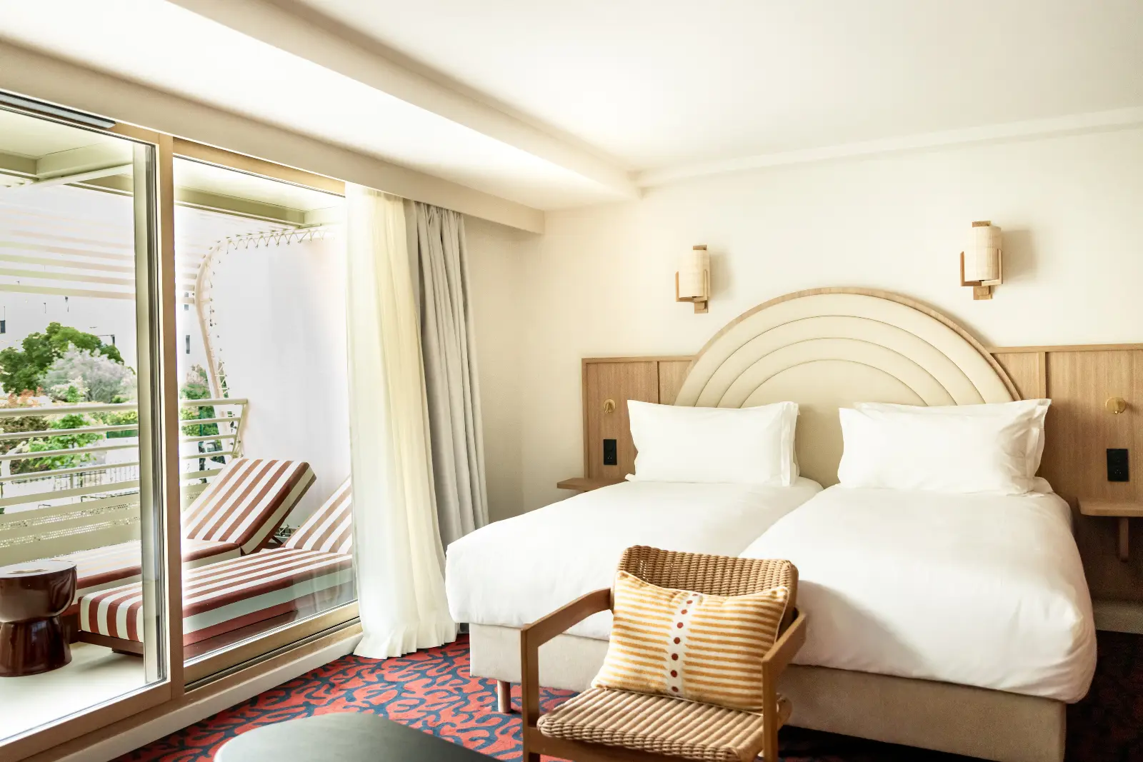 A bright twin hotel room with two single beds, a rattan armchair and a large bay window overlooking the greenery and hills