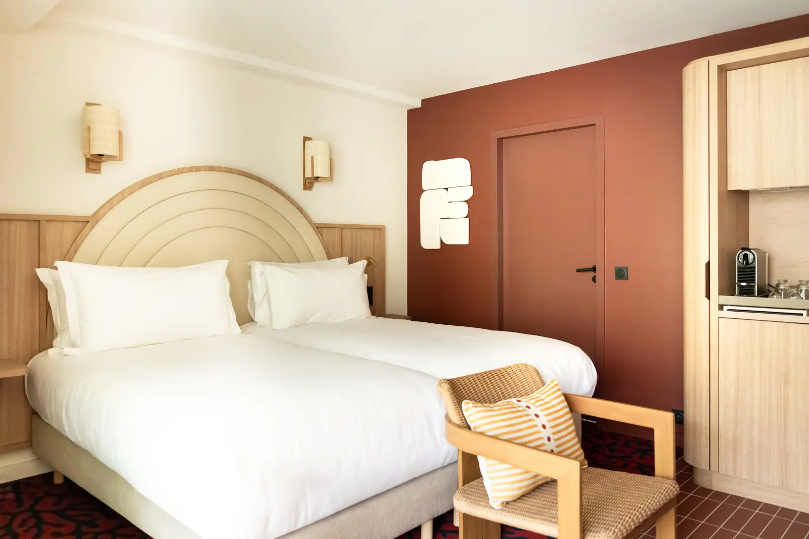 Hotel twin room with two single beds, a curved headboard, a terracotta feature wall and a rattan armchair