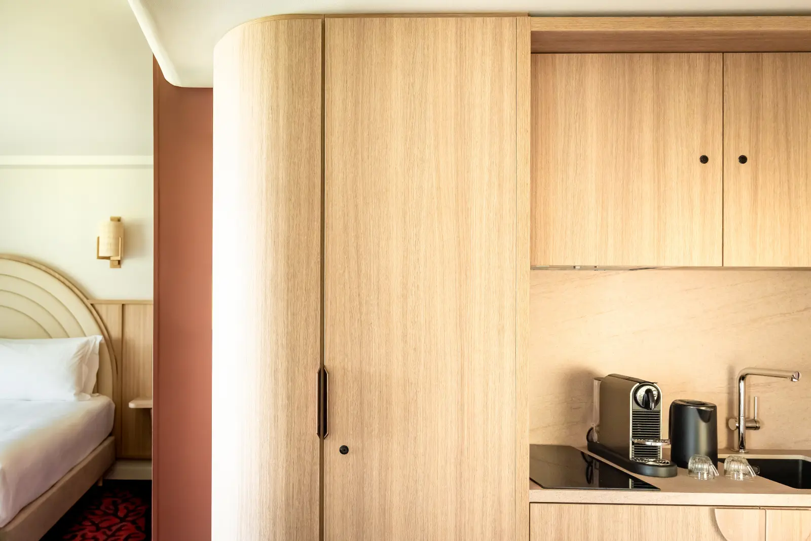 Built-in hotel kitchenette with light wood cupboards, a coffee machine and a chrome sink