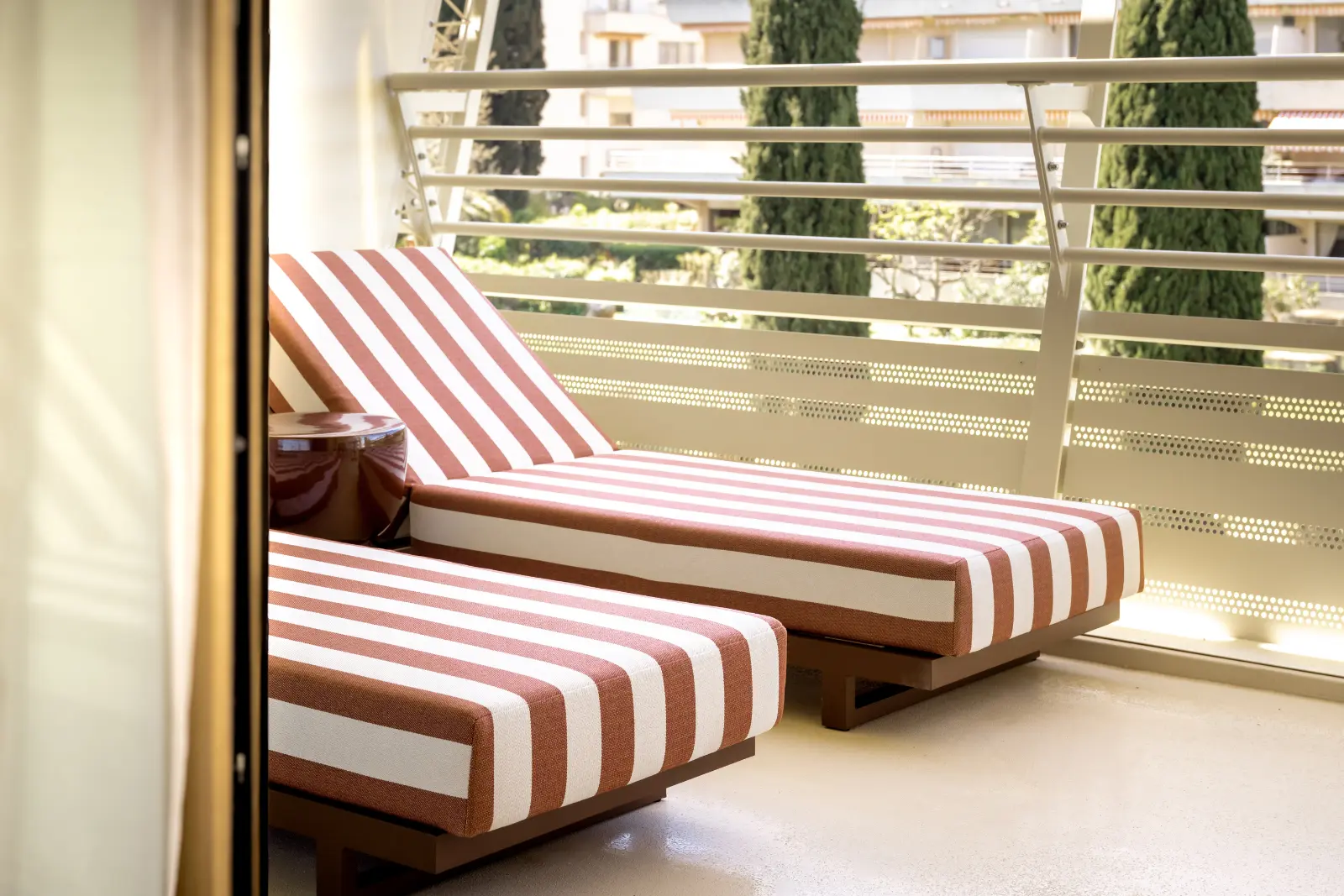Two terracotta-and-white striped sun loungers on a sunny balcony overlooking the greenery