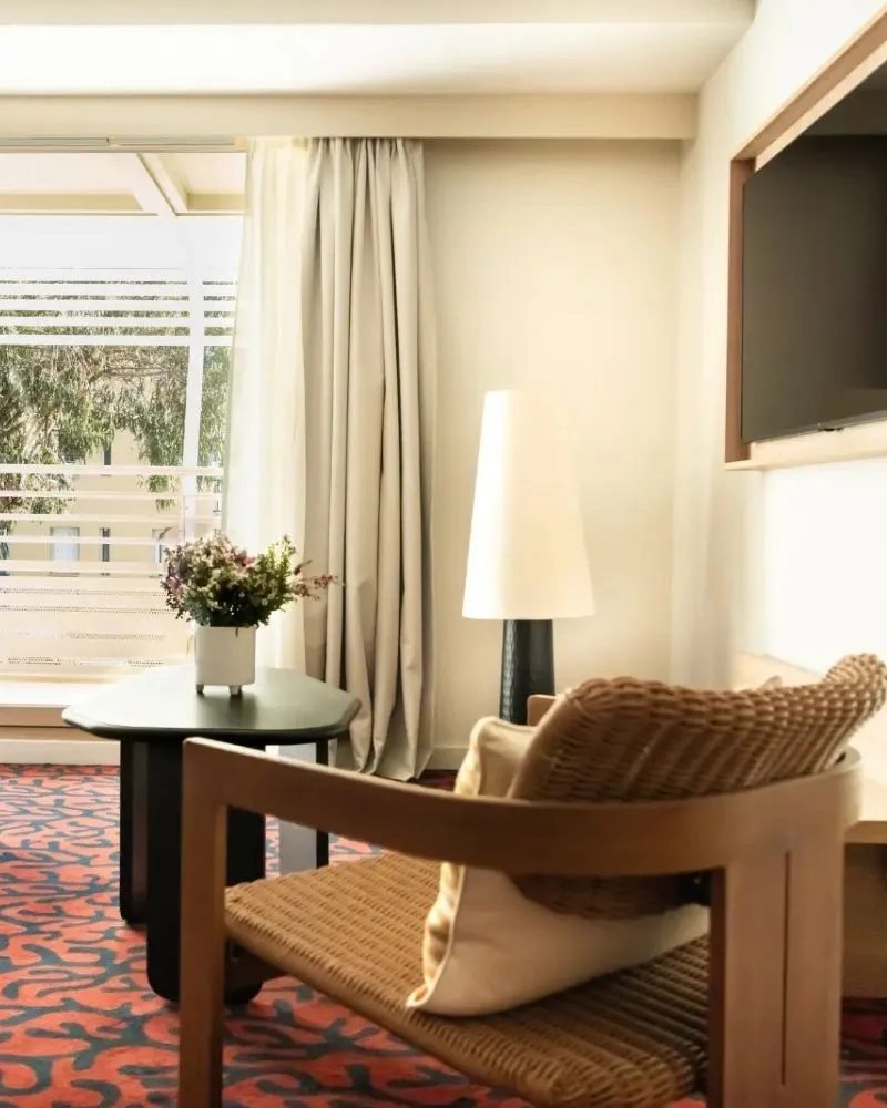 Salon d'une suite hôtelière avec canapé gris, bureau en bois et baie vitrée donnant sur la verdure