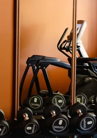 Salle de fitness d'hôtel avec rack d'haltères, vélos d'appartement et rameur sur fond de mur terracotta et miroir