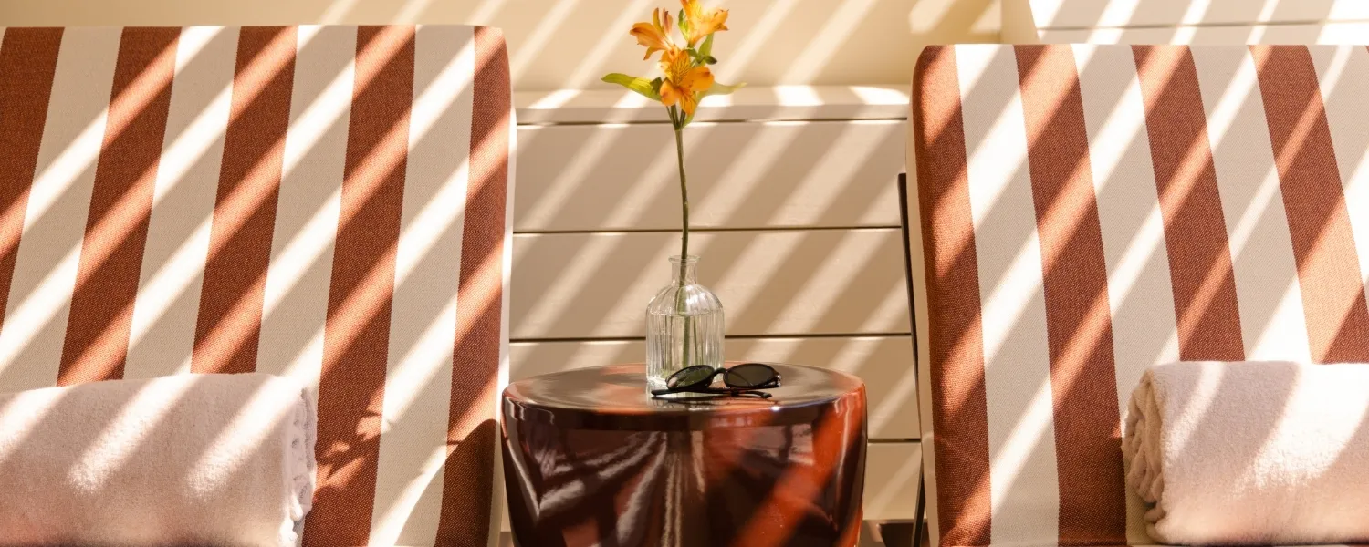 Serviettes de bain beiges roulées posées sur des transat à rayures terracotta et blanc au soleil