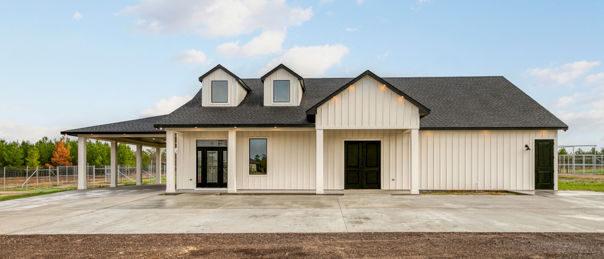 Modern white farmhouse with black roof, two dormer windows, and wide concrete driveway.
