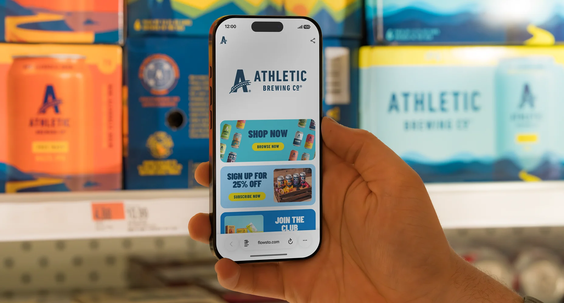 Hand holding smartphone displaying Athletic Brewing Co FlowHub with shop, discount, and club sign-up options.
