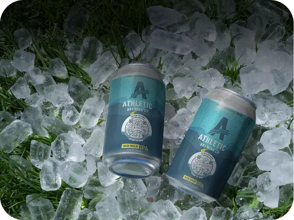 Two Athletic Brewing Co. Run Wild IPA cans with Flowcodes lying on ice over green grass.