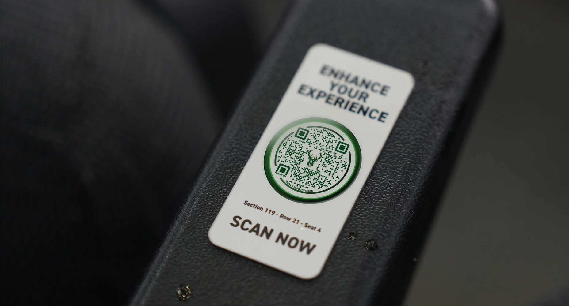Flowcode sear tag on black surface with text 'Enhance your experience' and seat info 'Section 119 - Row 21 - Seat 4'.