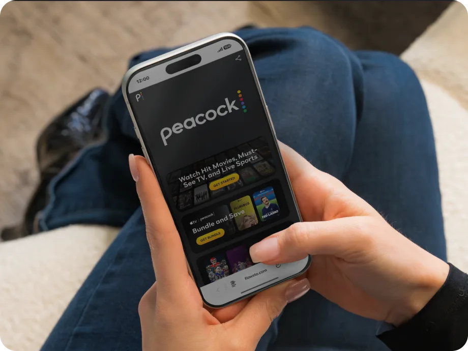Person holding a smartphone displaying the Peacock FlowHub homepage with options to get started and bundle offers.