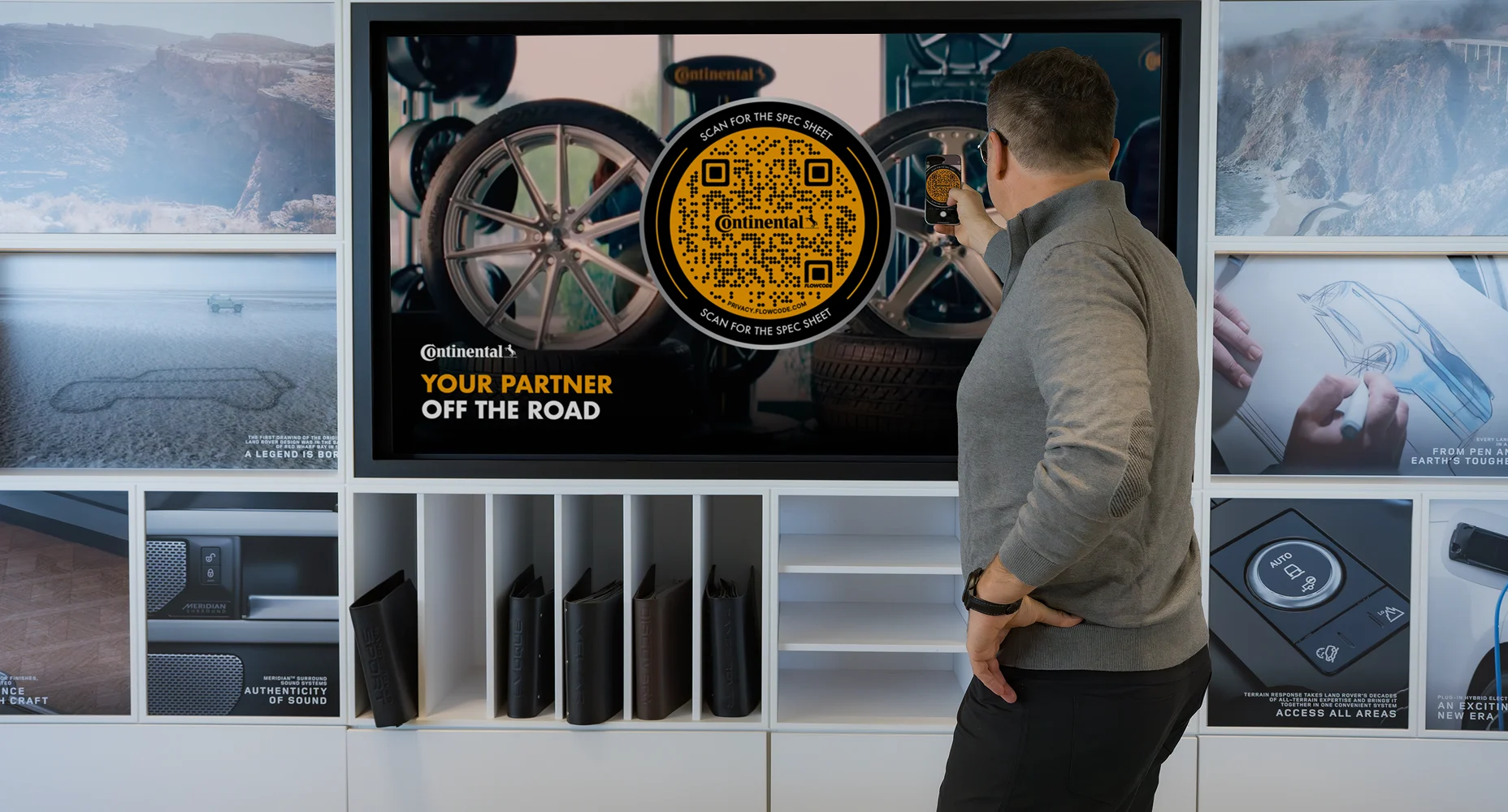 Man scanning a large Flowcode for Continental Tires displayed on a wall screen with car wheels in the background.