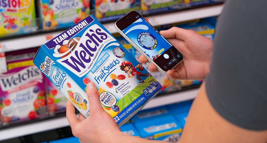 Person scanning a QR code on a Welch's Fruit Snacks Team Edition box with a smartphone in a store aisle.
