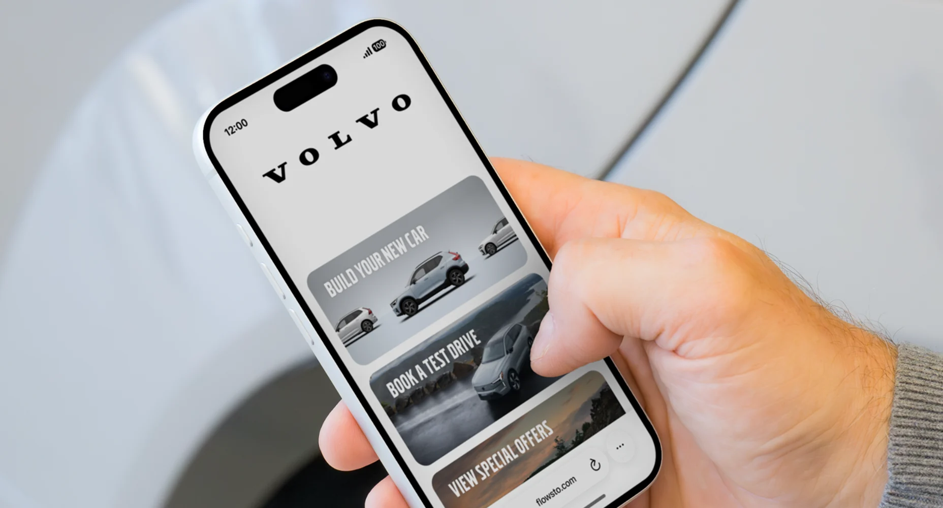 A person holding a smartphone showing a Volvo FlowHub with options to build a car, book a test drive, and view special offers.