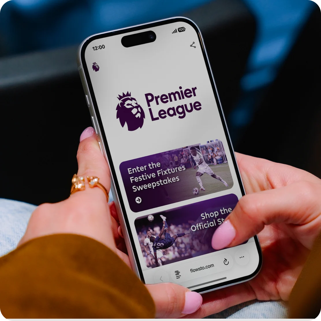 Person holding smartphone displaying Premier League FlowHub with with Festive Fixtures Sweepstakes and shop options.