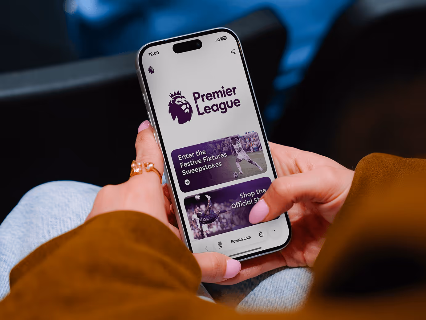 Person holding smartphone displaying Premier League FlowHub with with Festive Fixtures Sweepstakes and shop options.