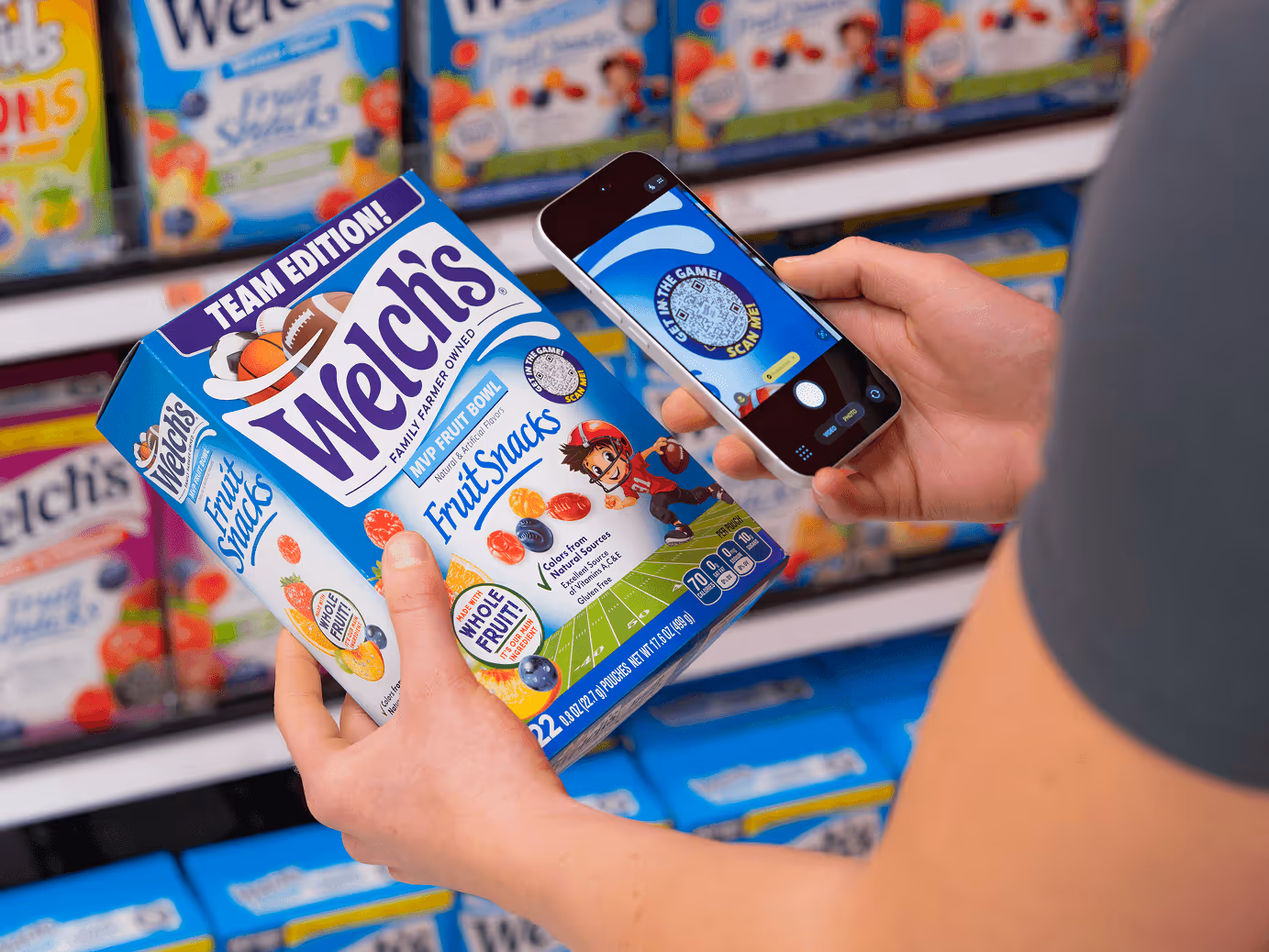 Person scanning a QR code on a Welch's Fruit Snacks box with a smartphone in a store aisle.