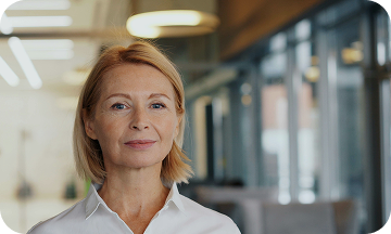 Smiling woman with short blonde hair and beard wearing a white collared shirt.