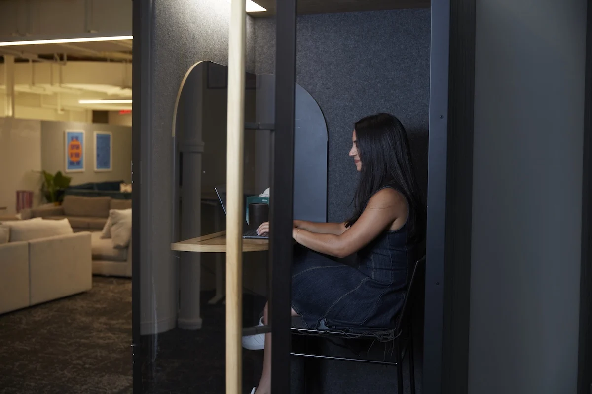 A Flowcode employee works in a phone booth within the office on her computer.