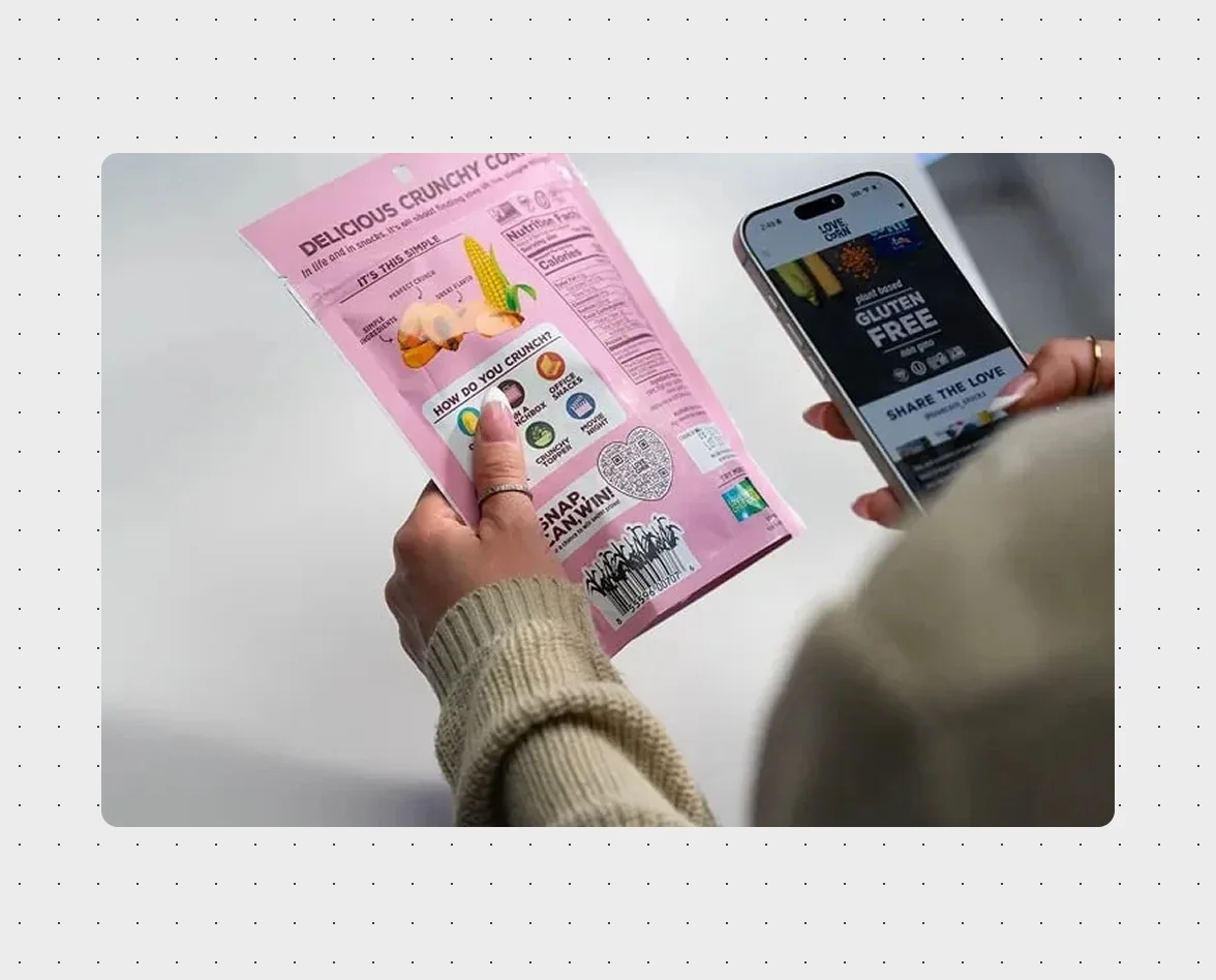 Consumer holding Love Corn snack packaging with a Flowcode on the back, with a phone displaying the brand's digital experience showing plant-based and gluten-free product information