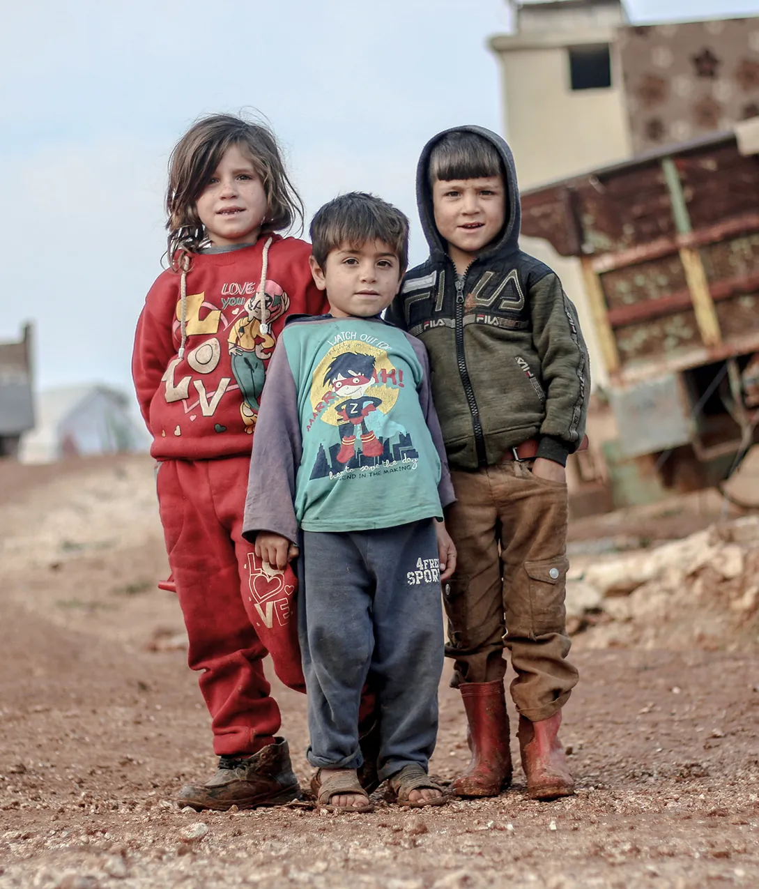 Three children standing together outdoors in a rural, dusty environment