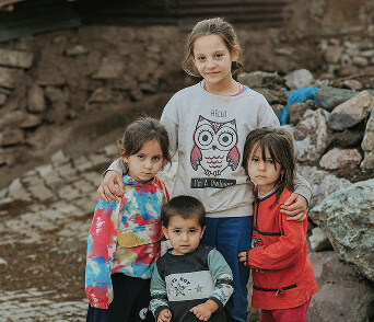 Four children standing together outdoors near a stone wall