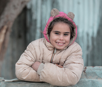 Girl in a winter coat and pink hat smiling with arms crossed