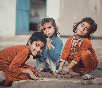 Three children in orange clothing sitting together outdoors