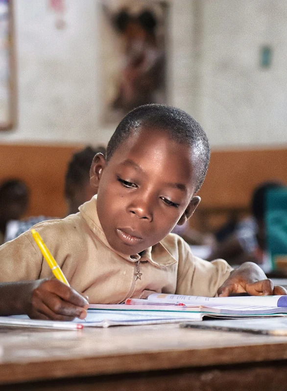 Child writing in a notebook with a pencil