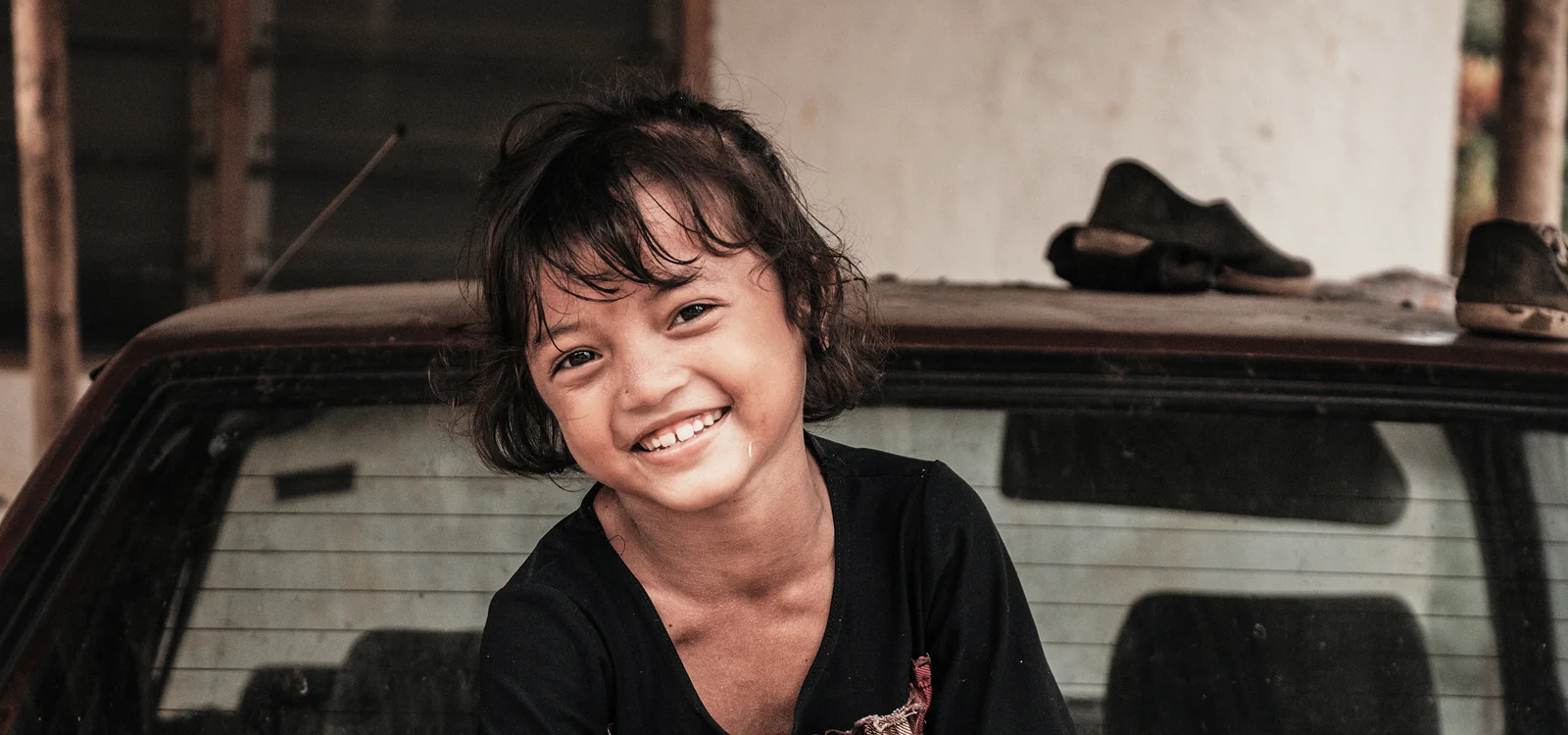 Smiling young girl sitting by an old car, representing giving with confidence to support children in need