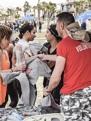 Volunteers in red shirts assisting participants with towels at a charity beach run