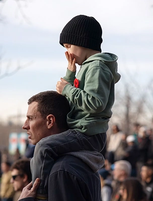 Child sitting on father's shoulders at an outdoor gathering, encouraging people to make a donation