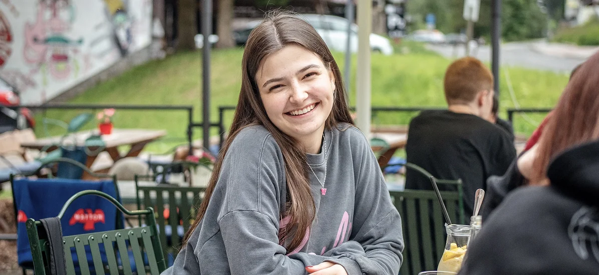 Smiling young woman sitting at an outdoor cafe table, illustrating how small actions create lasting impact