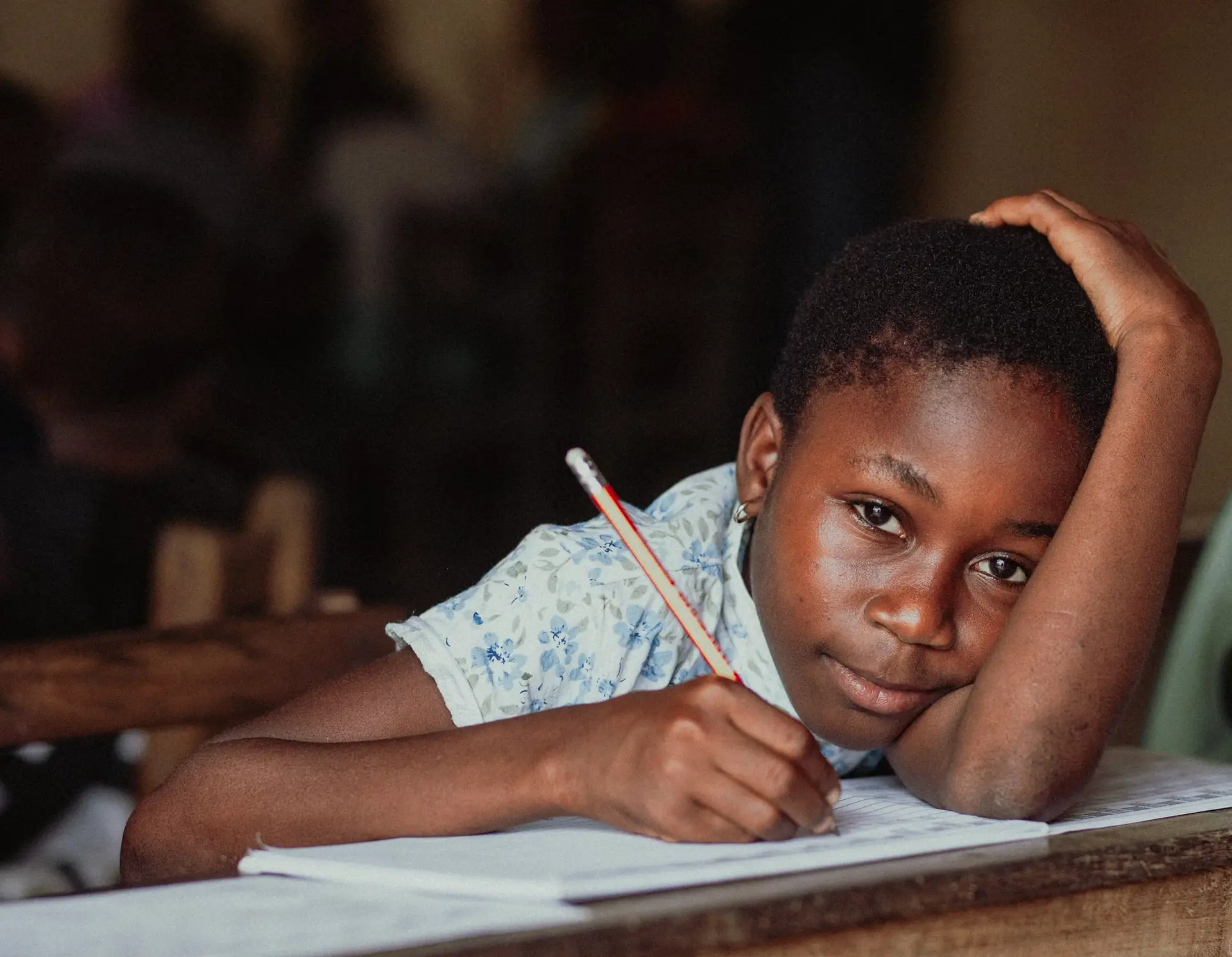 Young girl resting her head on her arm while writing with a pencil in a classroom