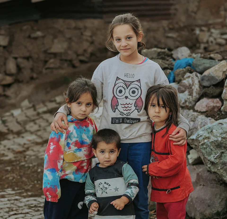 Four young siblings from a crisis-affected community standing together outdoors, embracing one another