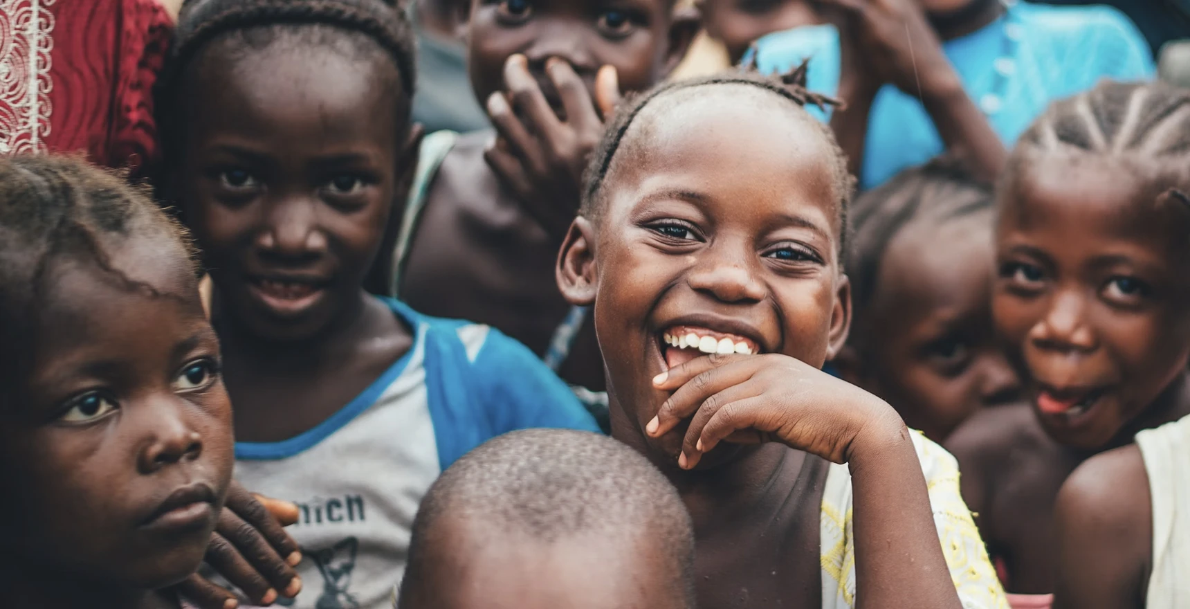 Group of smiling children close together outdoors, one laughing directly at the camera