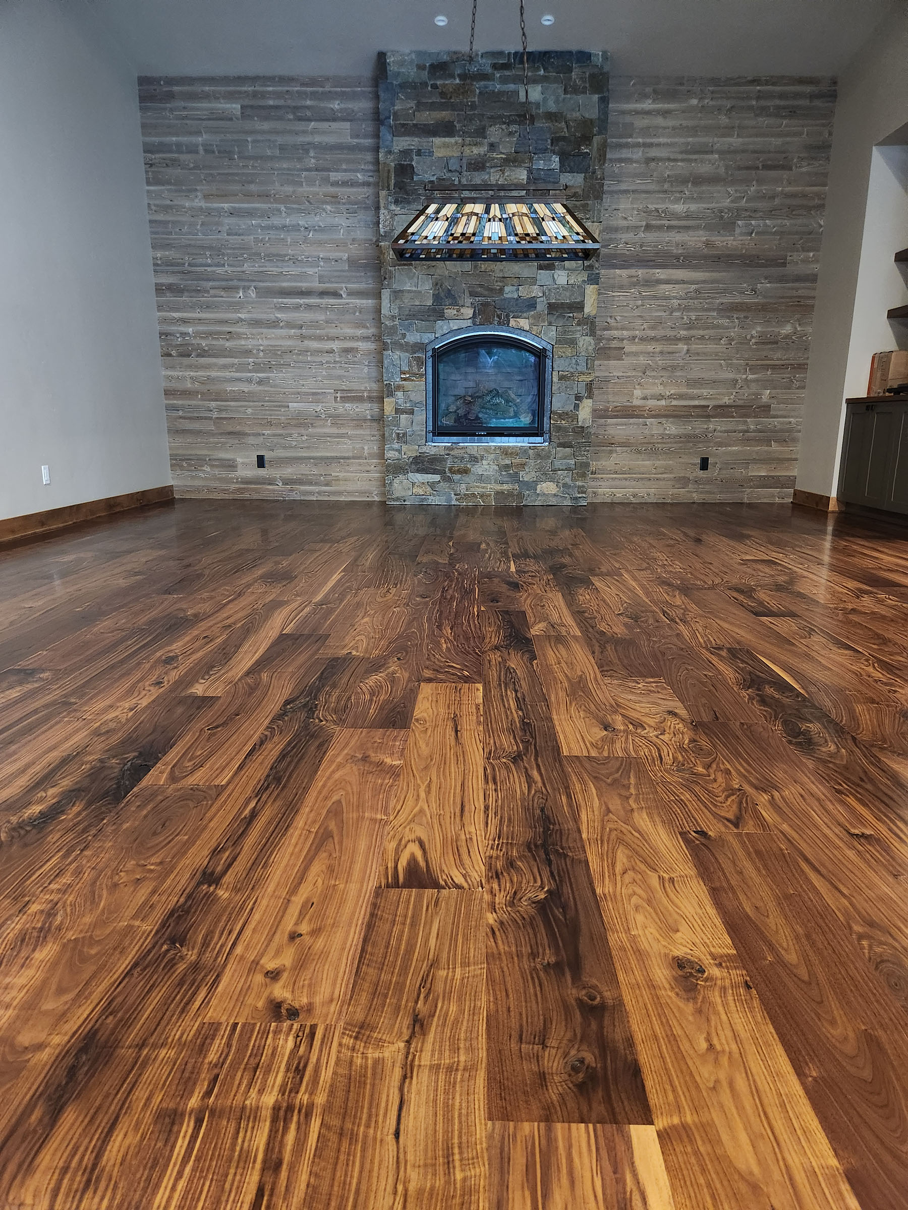 Room with polished wood floor, stone fireplace, wood plank wall, and stained glass pendant light.