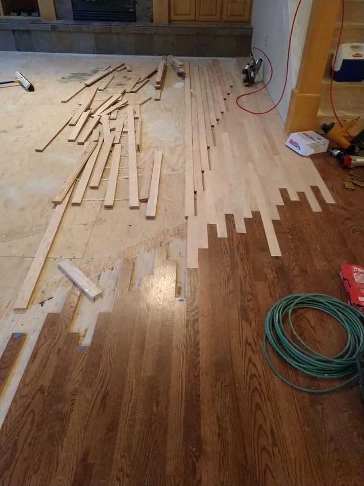 Partially installed hardwood floor with tools and wood planks scattered in a room under renovation.