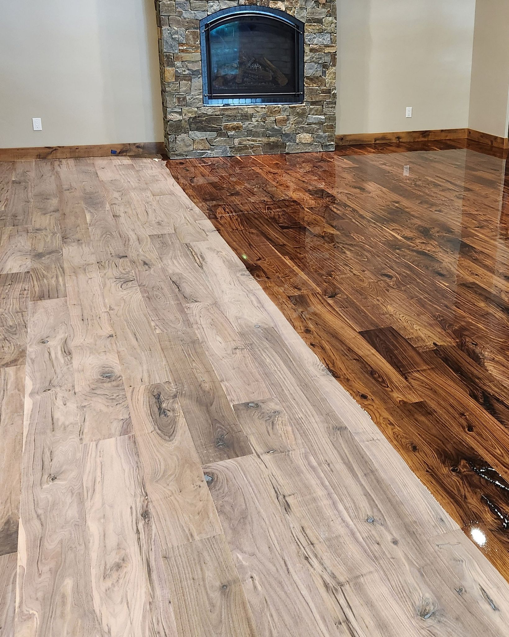 Room floor with half unfinished light wood and half glossy finished dark wood near stone fireplace.