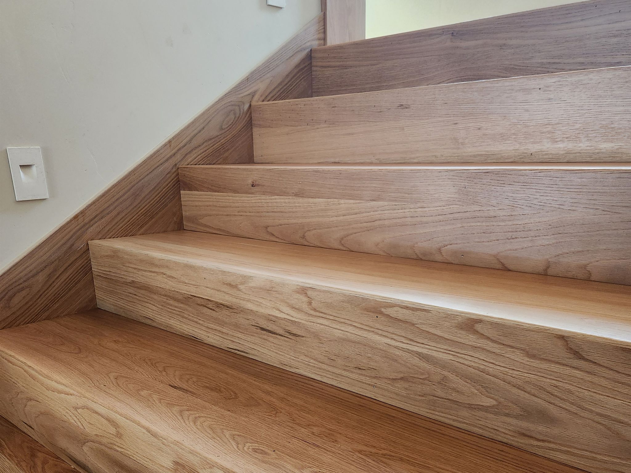 Close-up of wooden stairs with natural grain and smooth finish next to a beige wall.