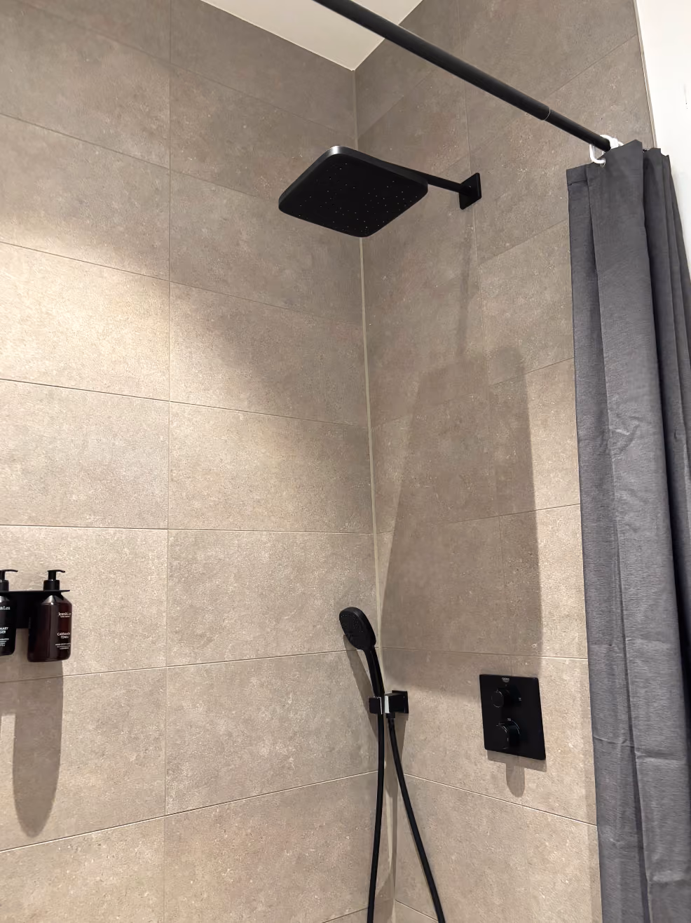 Modern bathroom shower with square black rain showerhead, handheld shower, and gray tiled walls.