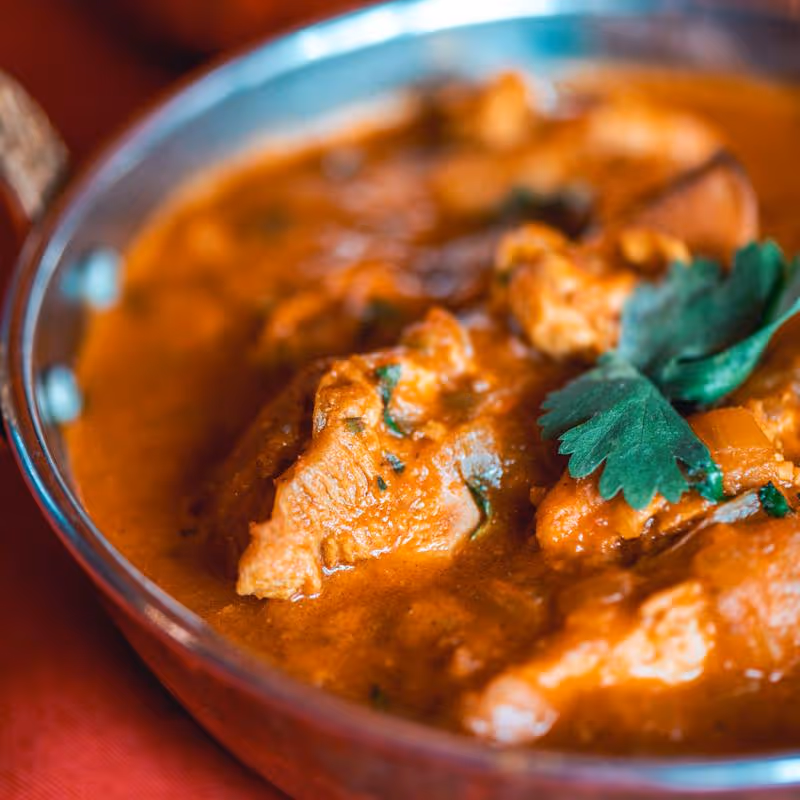 Close-up of chicken curry garnished with cilantro in a metal bowl.