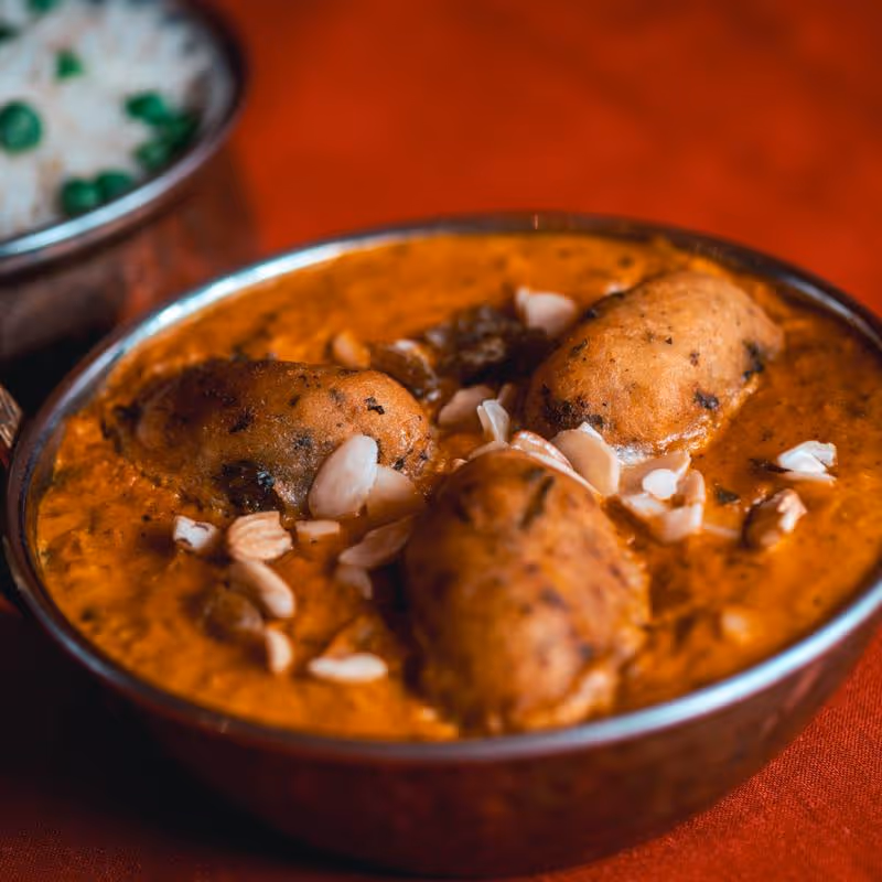 Indian curry dish with fried dumplings and garnished with almond slices in a metal bowl.