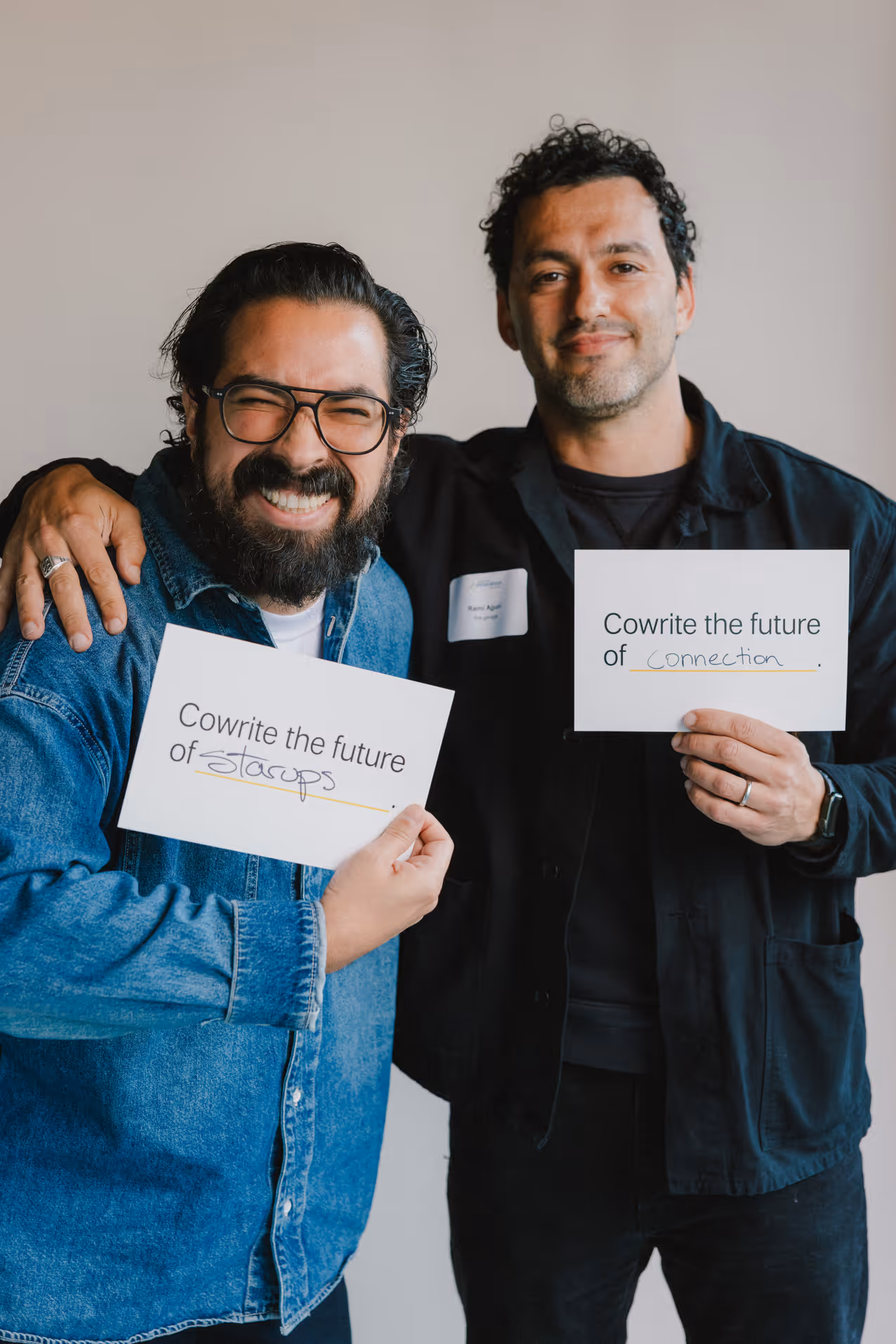 Two men smiling and holding cards reading 'Cowrite the future of startups' and 'Cowrite the future of connection.'