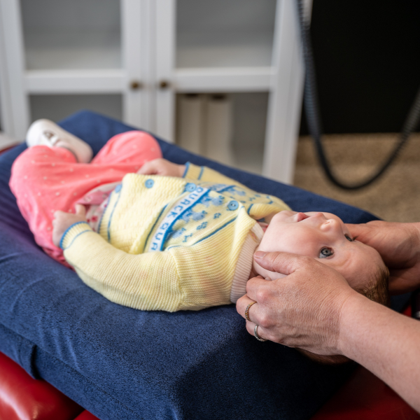 Baby lying on a blue cushioned surface with an adult gently supporting their head.
