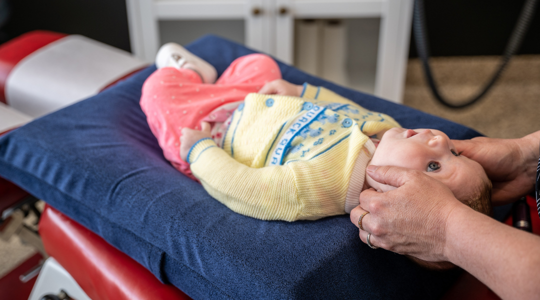 Baby lying on a blue cushioned surface with an adult gently supporting their head.