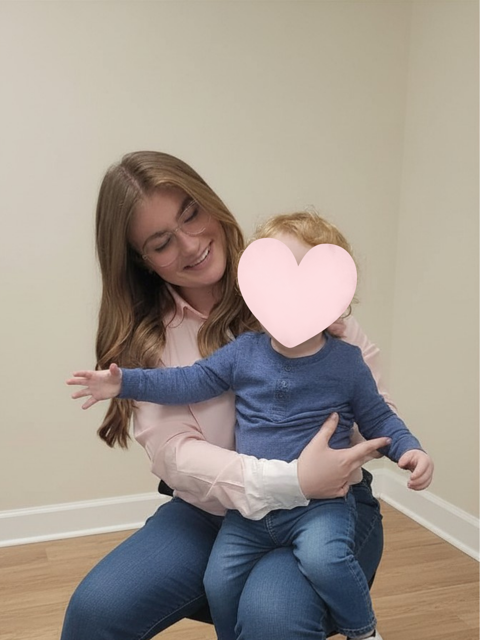 Woman with long hair and glasses holding a toddler wearing a blue shirt and jeans, sitting on her lap.