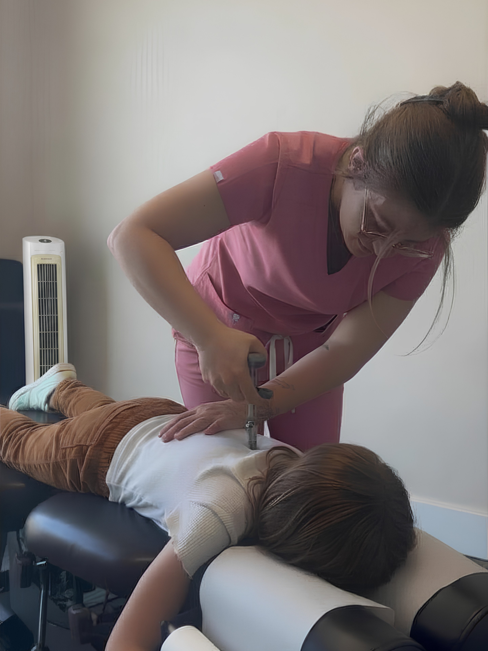 Chiropractor in pink scrubs performing spinal adjustment on a child lying face down on a treatment table.