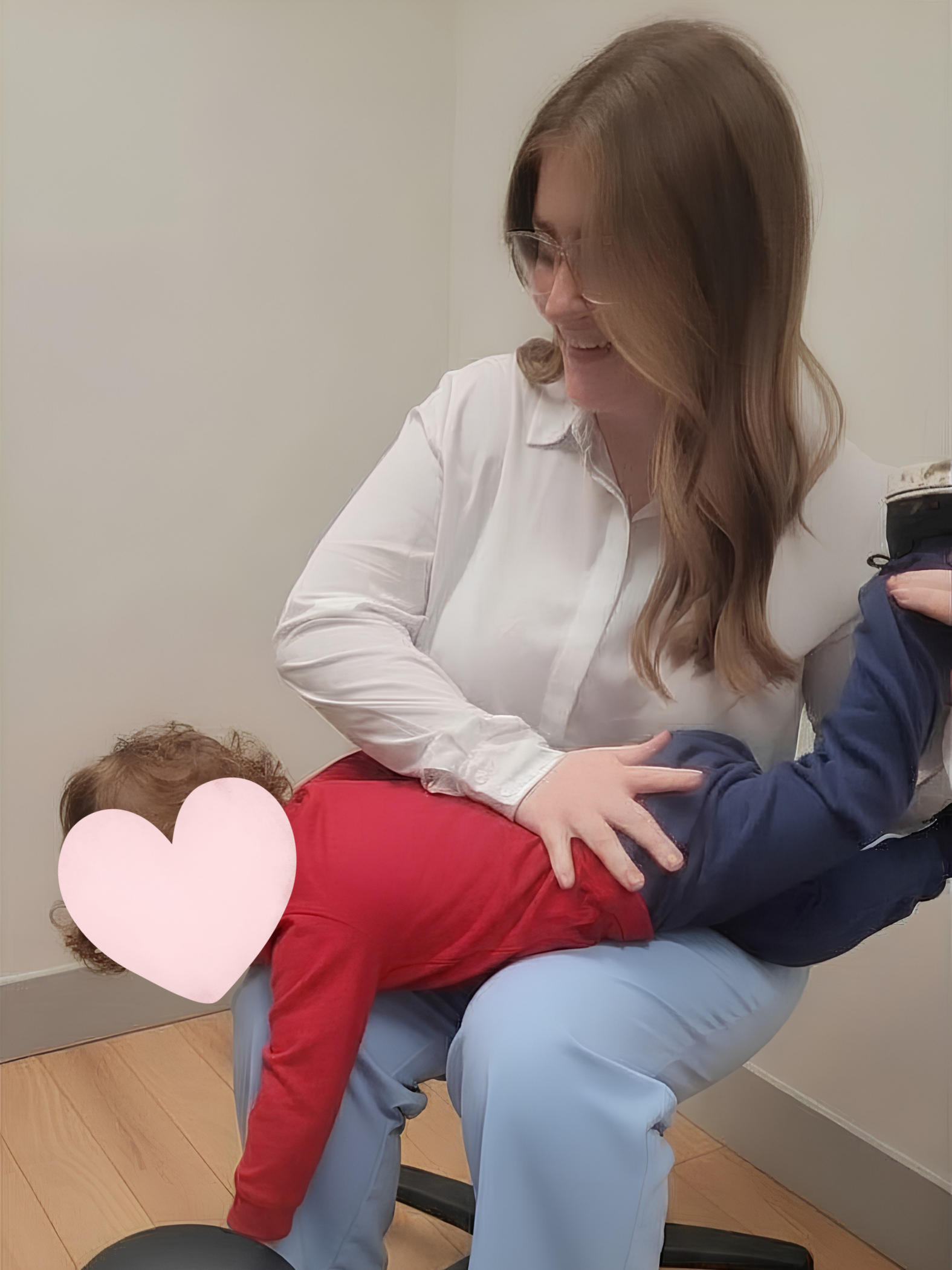 Woman with glasses holding a child dressed in red and blue, smiling in a light-colored room.