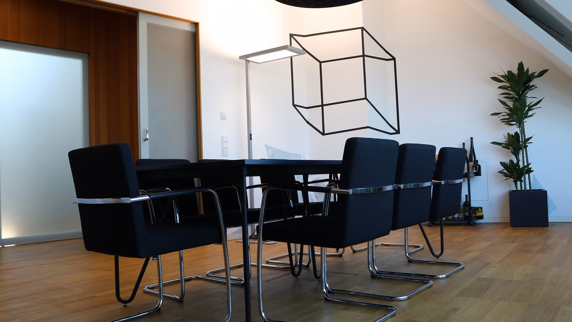 Modernes, minimalistisches Esszimmer mit schwarzem Tisch und Stühlen, geometrischer Pendelleuchte, Holzboden und Topfpflanzen, die für eine ruhige Atmosphäre sorgen.
